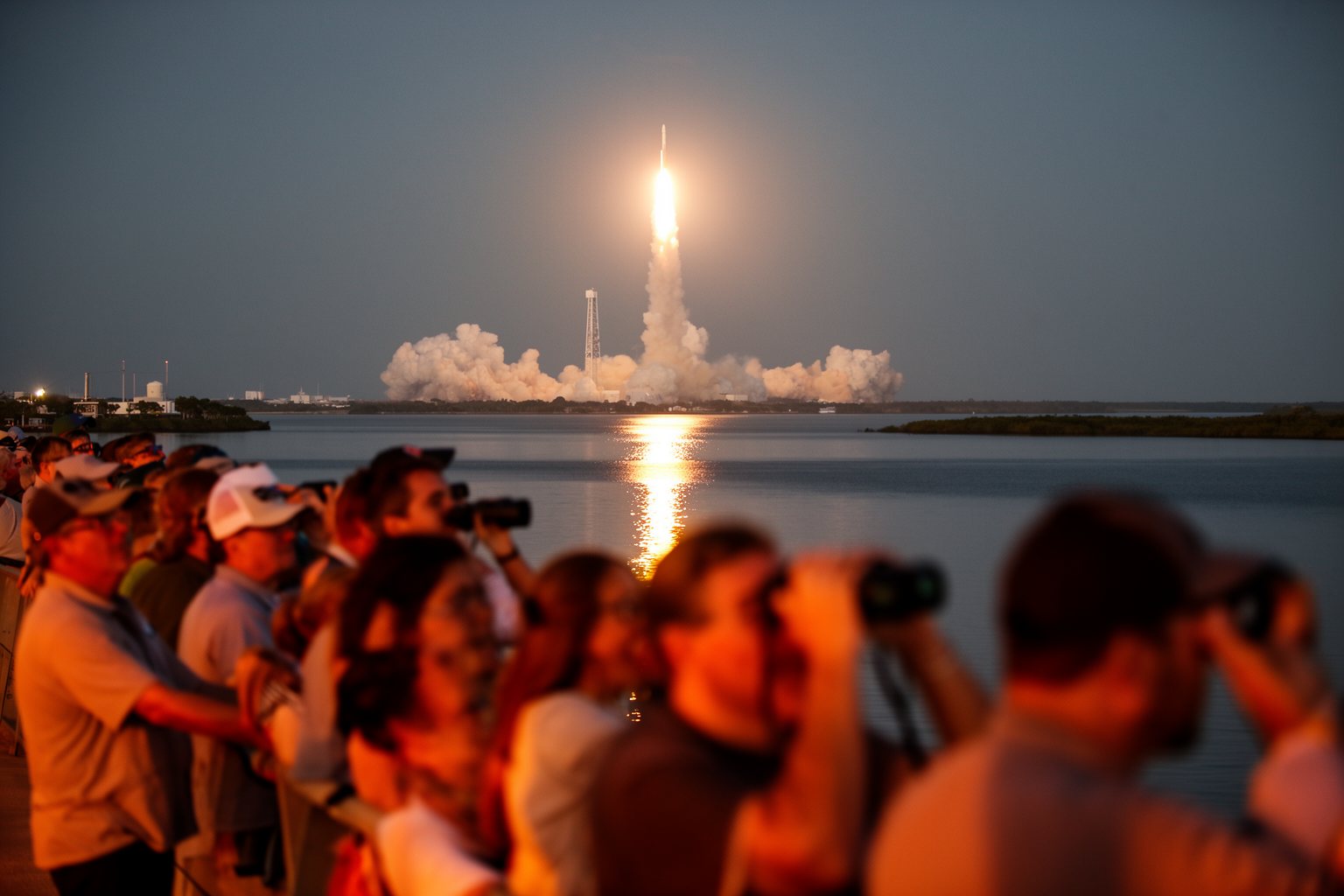 Spectators on a Florida causeway watching a rocket launch from the Space Coast at dawn