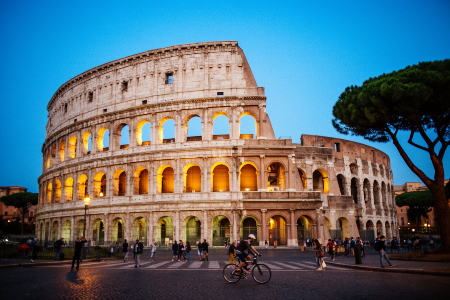 The Colosseum in Rome at dusk with people walking on the street below