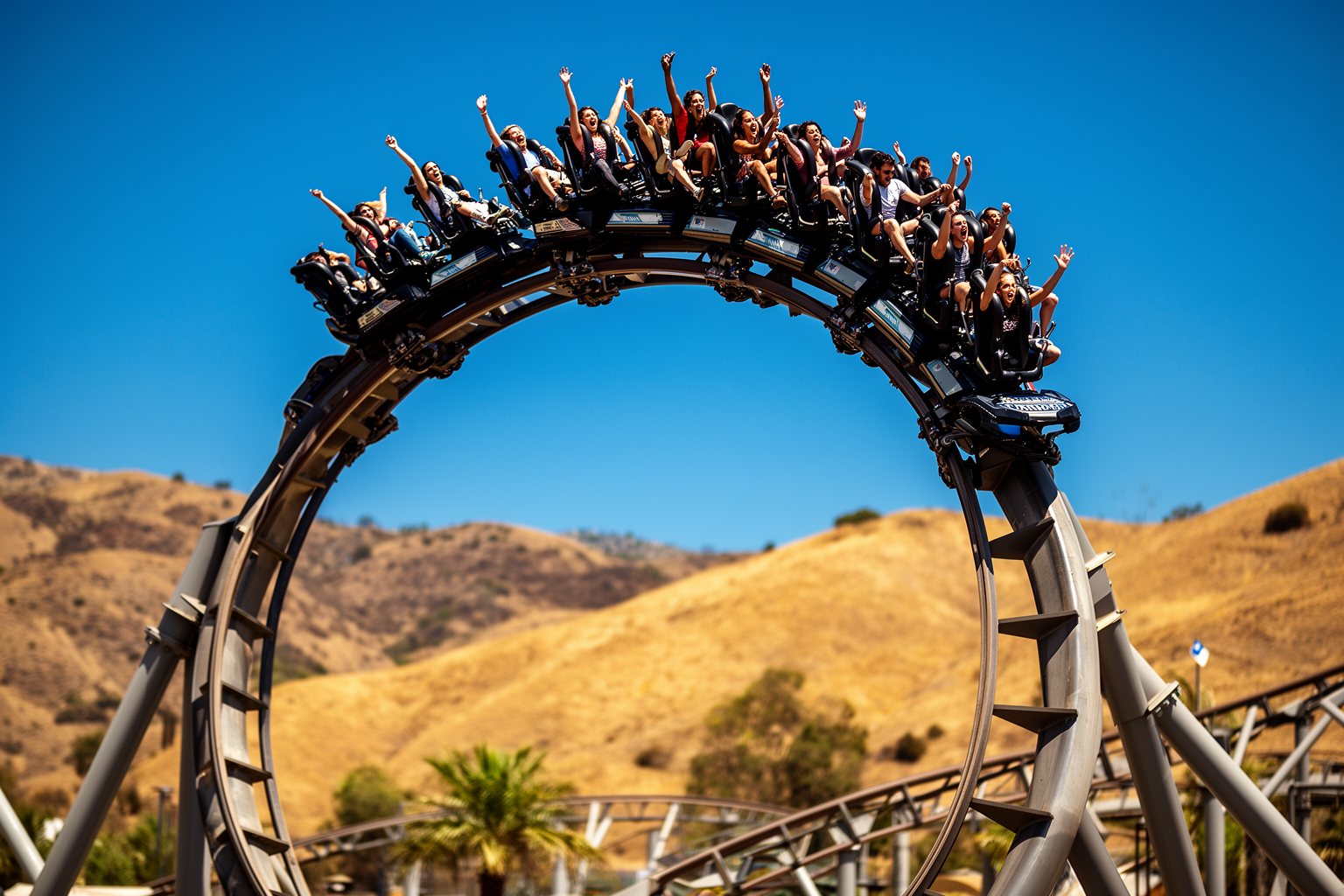 5 Best Family-Friendly Theme Parks Near Los Angeles Riders with arms up on a towering steel roller coaster loop at a thrill park north of Los Angeles