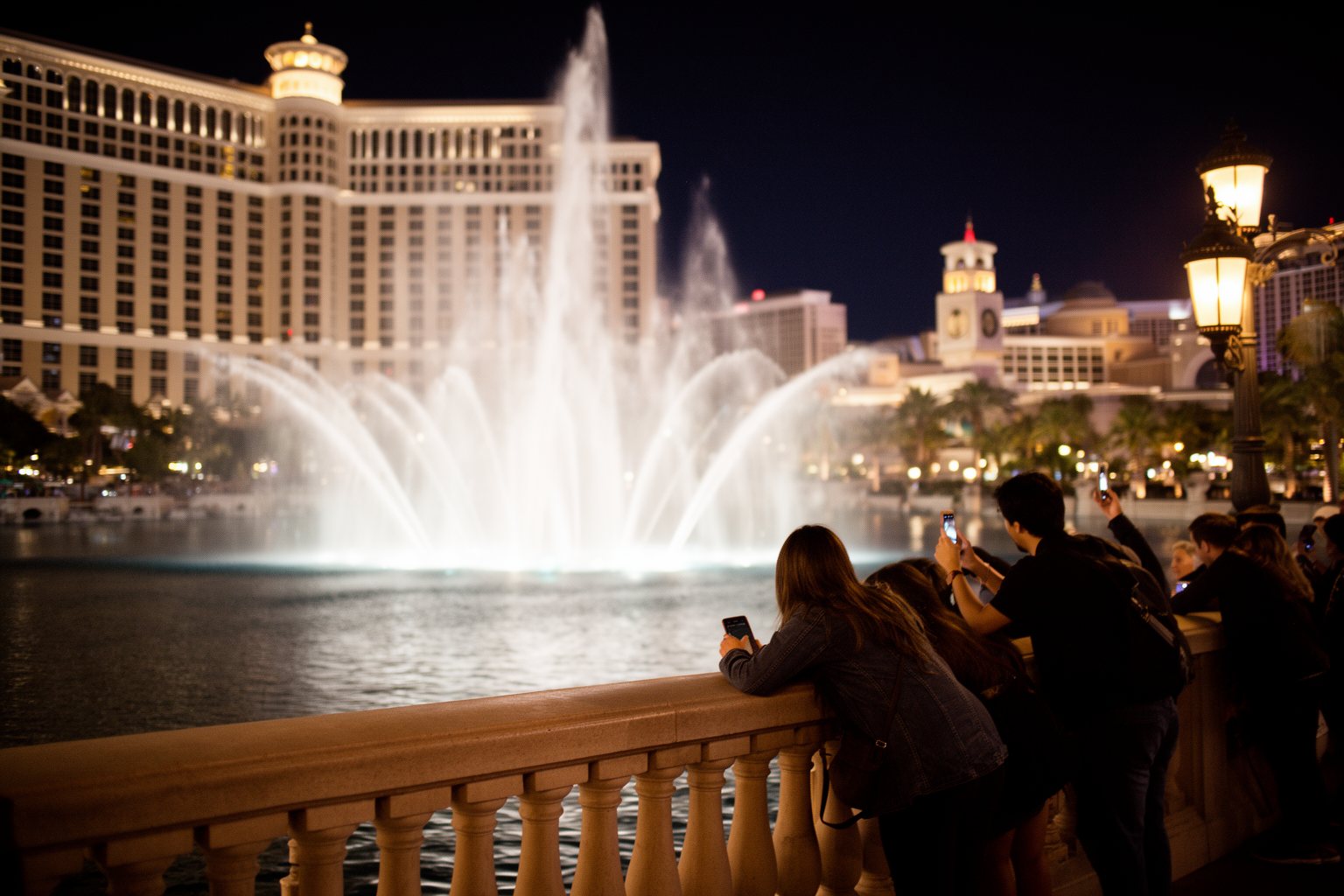 Vegas Nightlife Guide: Clubs, Shows, Casinos and Late Eats Visitors at a railing watching a dancing fountain show in front of a Las Vegas Strip resort at night