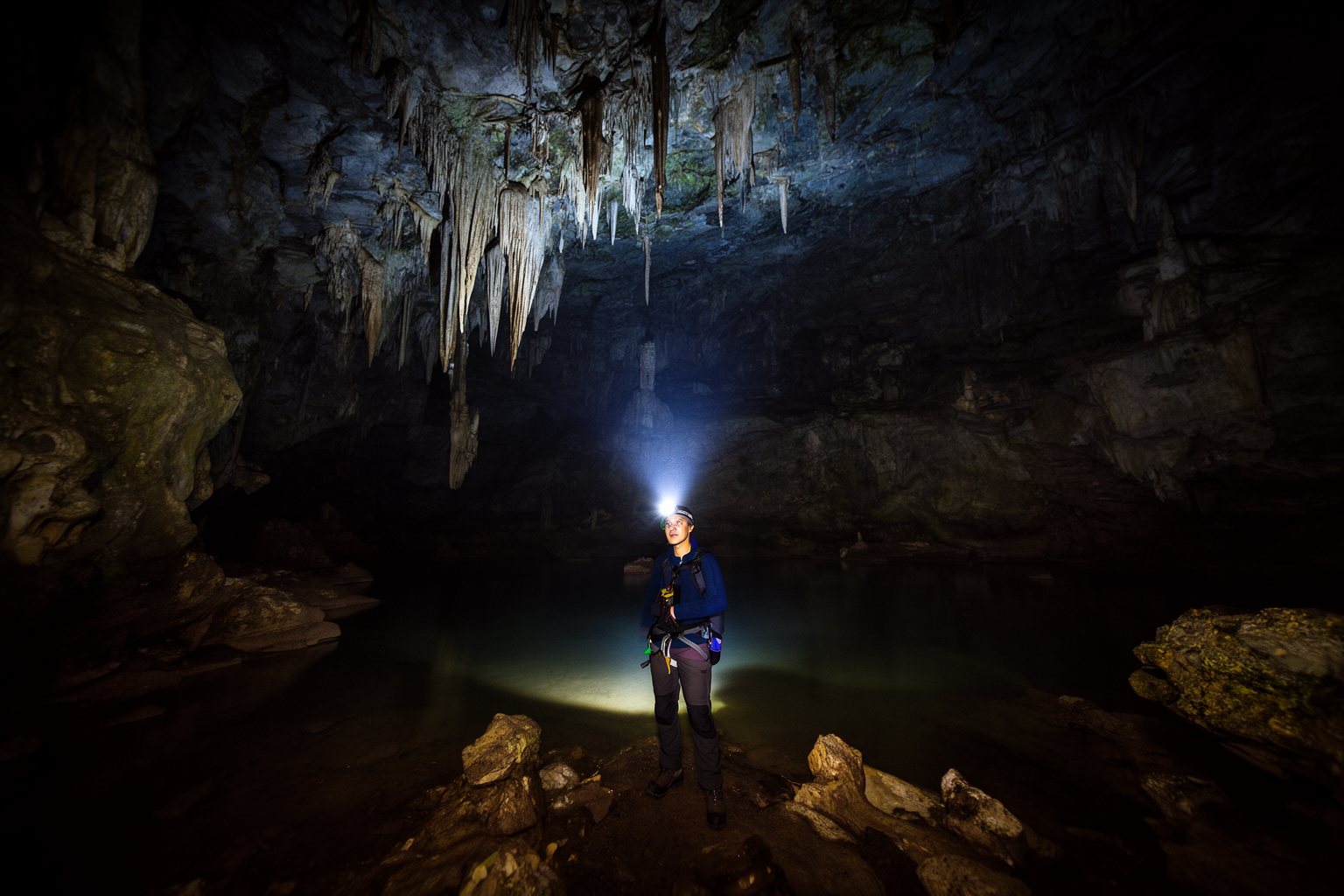 Explorer with a headlamp in a vast dark cave, evoking an atmospheric indie adventure