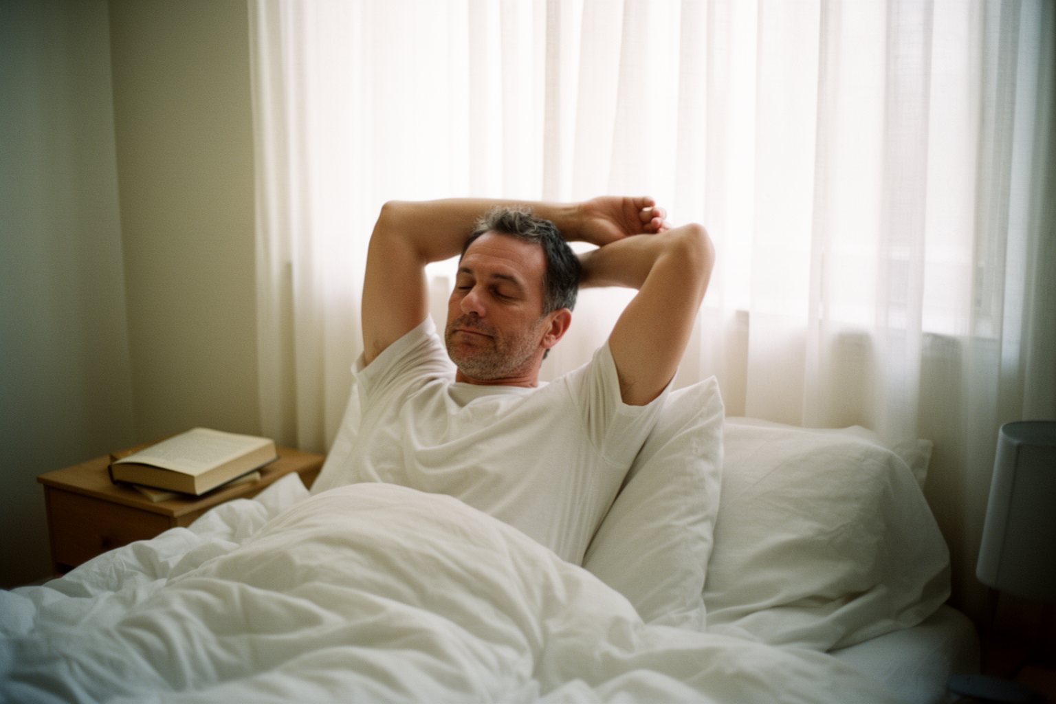 Hacking Your Sleep For A Restful Night Man waking up refreshed in the morning, sitting up in bed in soft daylight