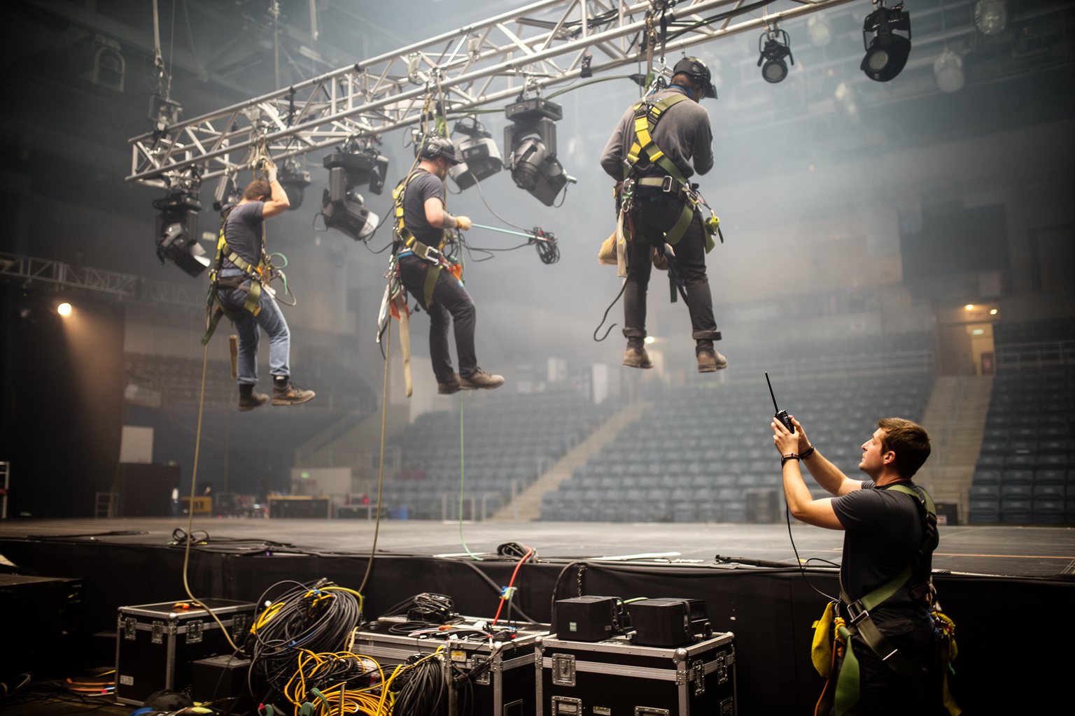 Entertainment Industry Behind the Scenes: Hidden Faces Crew members rigging lights on a concert truss above an empty arena stage