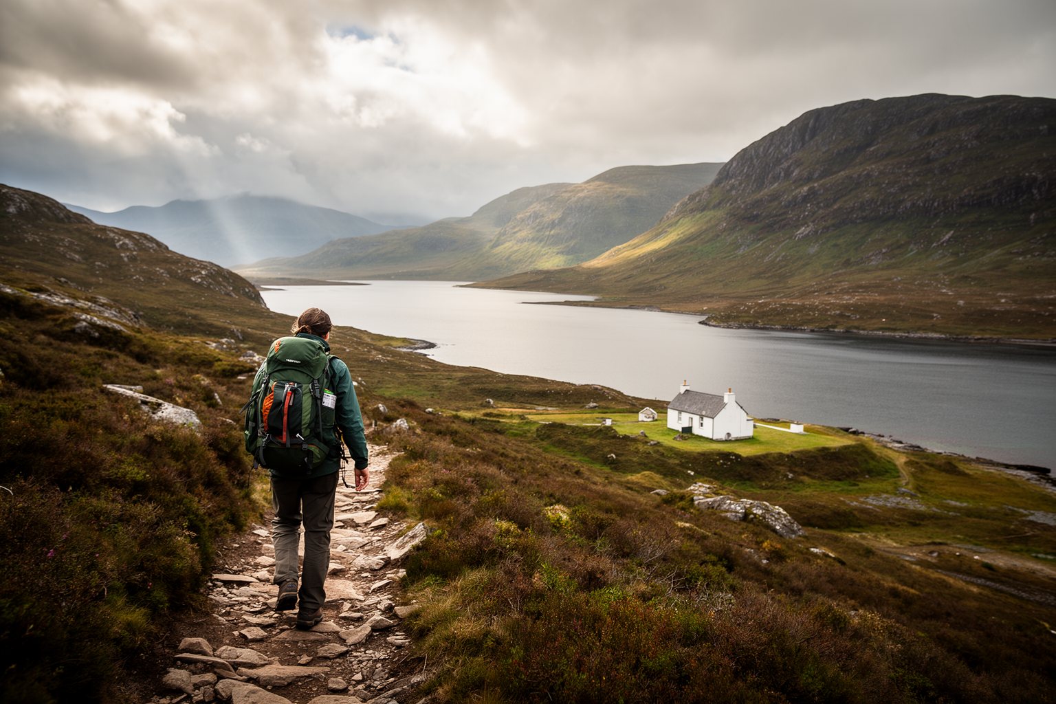 10 Secret Destinations Only Travel Pros Know Hiker on a trail above a loch and rugged hills in the Knoydart wilderness, Scotland