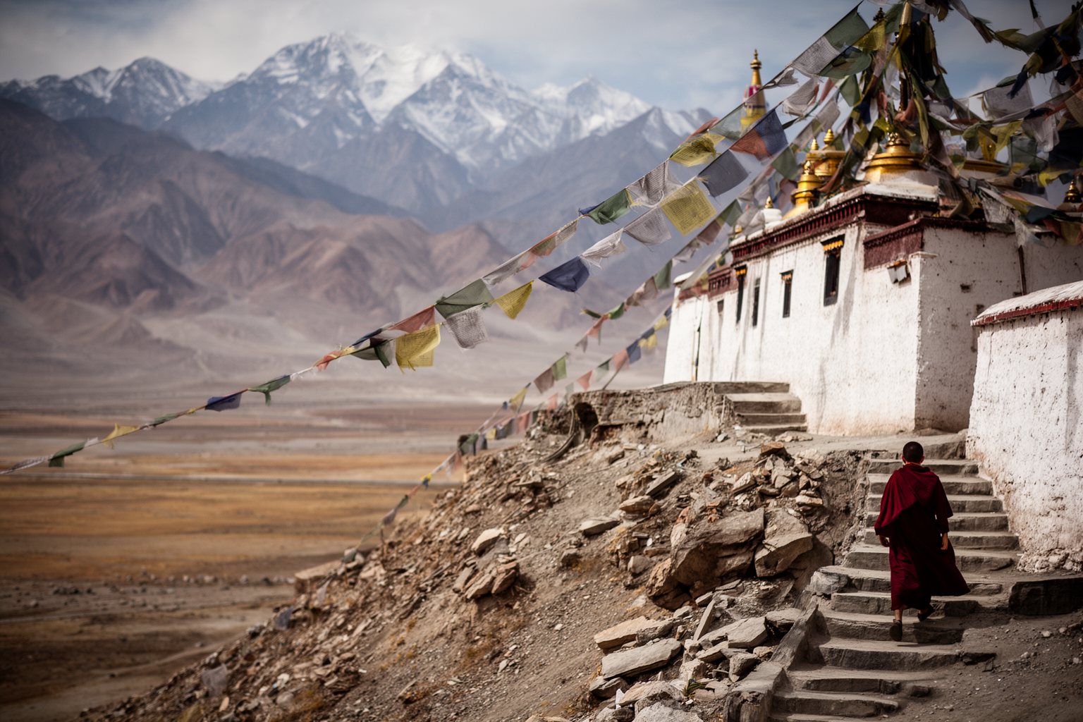 10 Secret Destinations Only Travel Pros Know Buddhist monastery with prayer flags against the Himalayan peaks near Leh, Ladakh