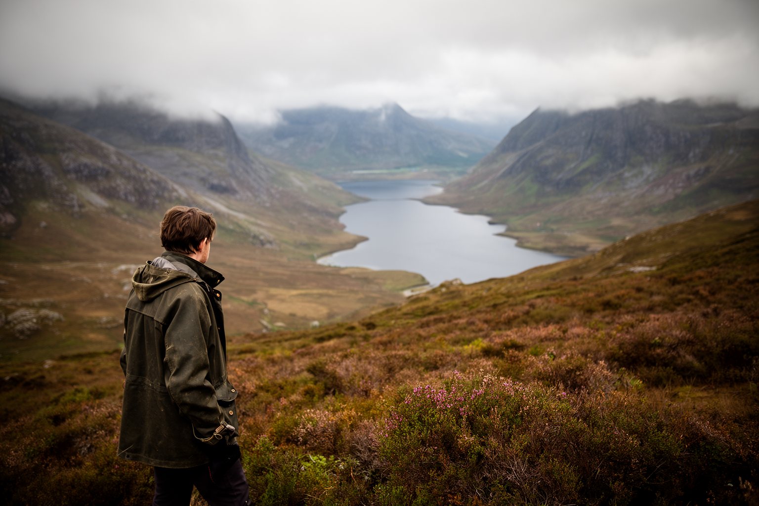 Walker in the Scottish Highlands looking over a heather-covered glen and a loch