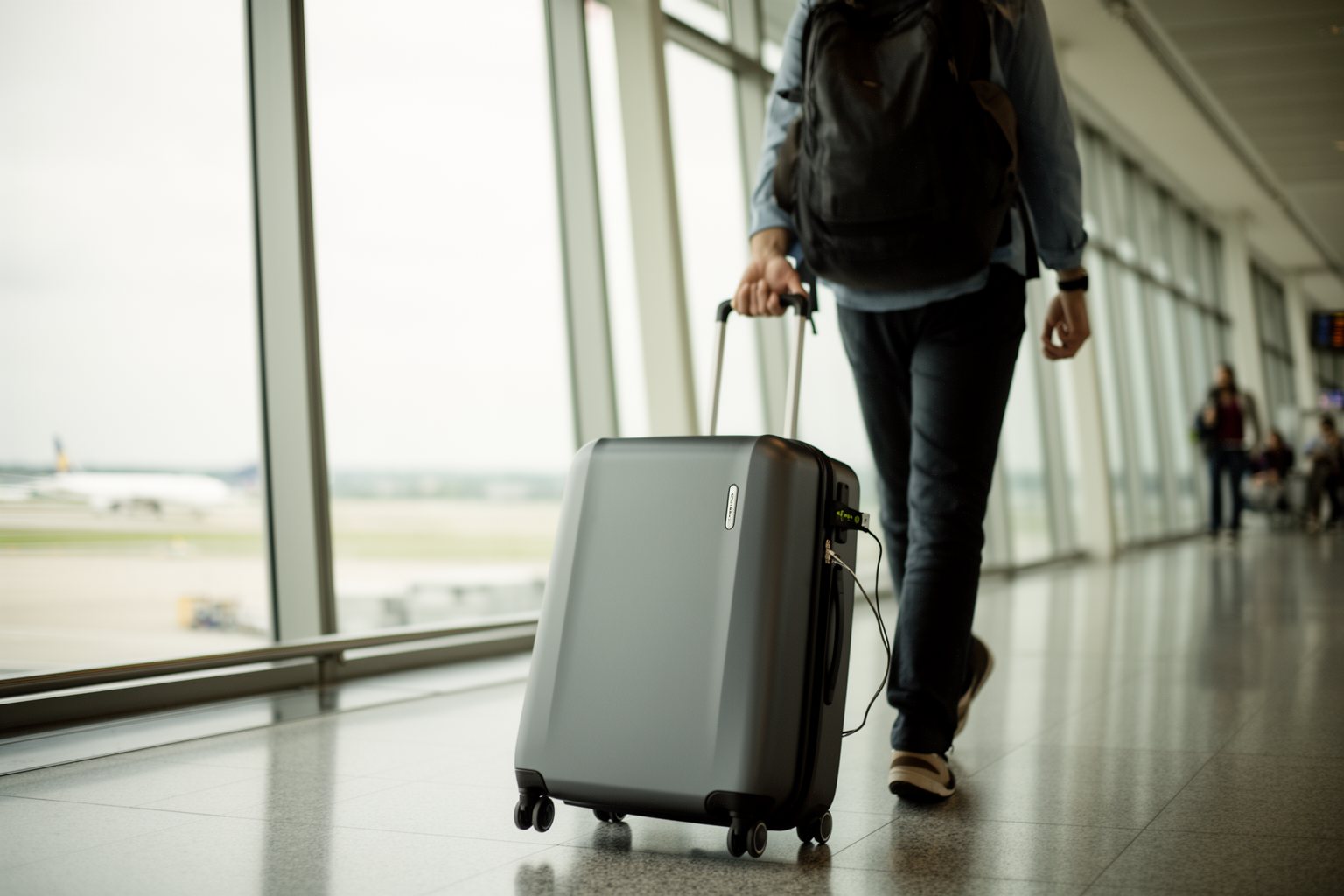 Unveiling The Top 10 Travel Gadgets You Never Knew You Needed Traveler rolling a hard-shell smart suitcase through a bright airport terminal
