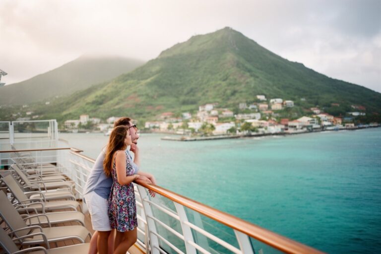 CruiseCompete Review: How to Get the Best Cruise Price Couple on a cruise ship deck watching a Caribbean island approach, a cruise deal well booked