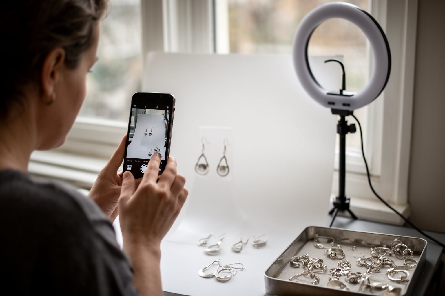 Maker photographing handmade jewellery with a phone for a social media post
