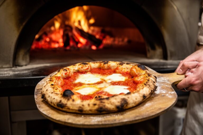 Why Is Pizza Round? The Science and History of the Shape Round pizza on a wooden peel just out of a wood-fired oven