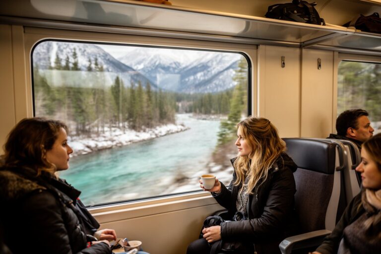 Riding the Rails: Unforgettable Train Journeys Around the World Passengers watching snowy mountains and a valley from the panoramic window of a scenic train