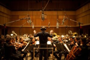 A Symphony of Emotions: The Invisible Power of Music in Film Orchestra recording a film score on a scoring stage as a conductor leads the musicians