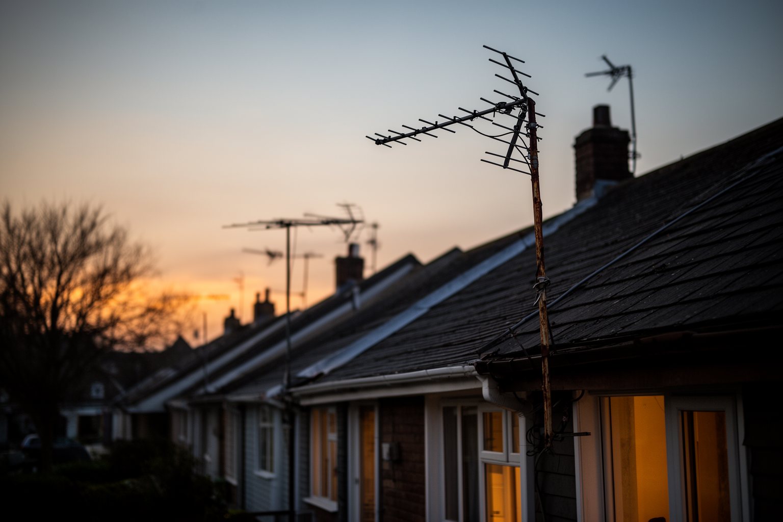 Streaming vs Traditional Television: Who Is Winning? Row of suburban rooftops with old TV antennas silhouetted against a dusk sky