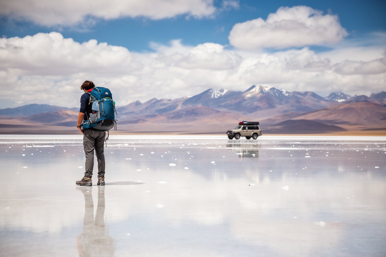 10 Budget-Friendly Backpacker Destinations to Explore Backpacker standing on the mirror-like Salar de Uyuni salt flat in Bolivia with Andes peaks behind